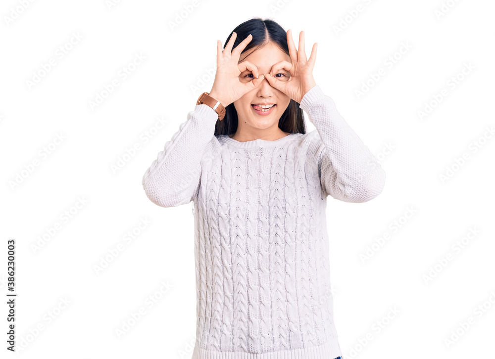 Young beautiful chinese woman wearing casual sweater doing ok gesture like binoculars sticking tongue out, eyes looking through fingers. crazy expression. Young beautiful chinese woman wearing casual sweater doing ok gesture like binoculars sticking tongue out, eyes looking through fingers. crazy expression.
