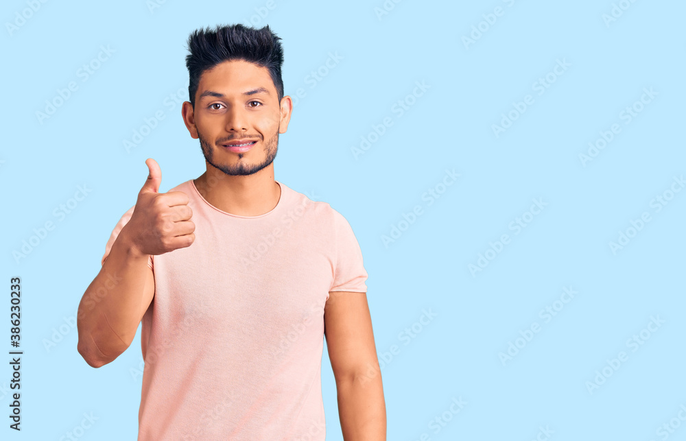 Handsome latin american young man wearing casual clothes smiling happy and positive, thumb up doing excellent and approval sign Handsome latin american young man wearing casual clothes smiling happy and positive, thumb up doing excellent and approval sign