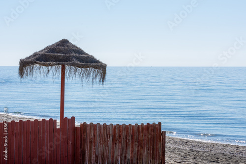 Beach umbrellas behind a red wooden fence on a sunny autumn day