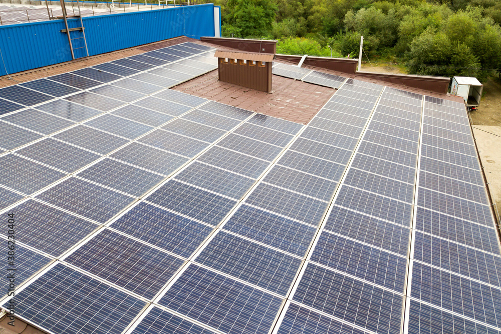 Aerial view of solar power plant with blue photovoltaic panels mounted of industrial building roof.