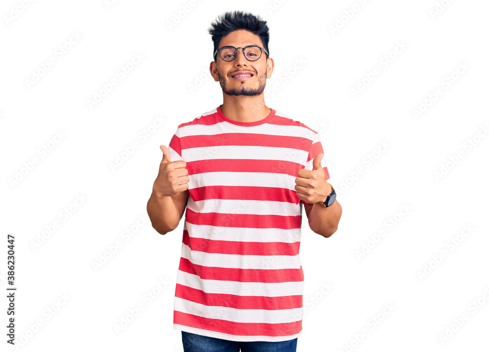 Handsome latin american young man wearing casual clothes and glasses success sign doing positive gesture with hand, thumbs up smiling and happy. cheerful expression and winner gesture. Handsome latin american young man wearing casual clothes and glasses success sign doing positive gesture with hand, thumbs up smiling and happy. cheerful expression and winner gesture.