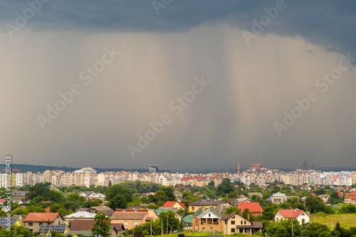 Vászonkép Moody landscape with dark stormy clouds with falling heavy downpour shower rain over distant town buildings in summer