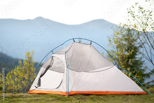 Empty camping tent standing on campsite with view of majestic high mountain peaks in distance. Hiking in wild nature and active trail travelling concept.