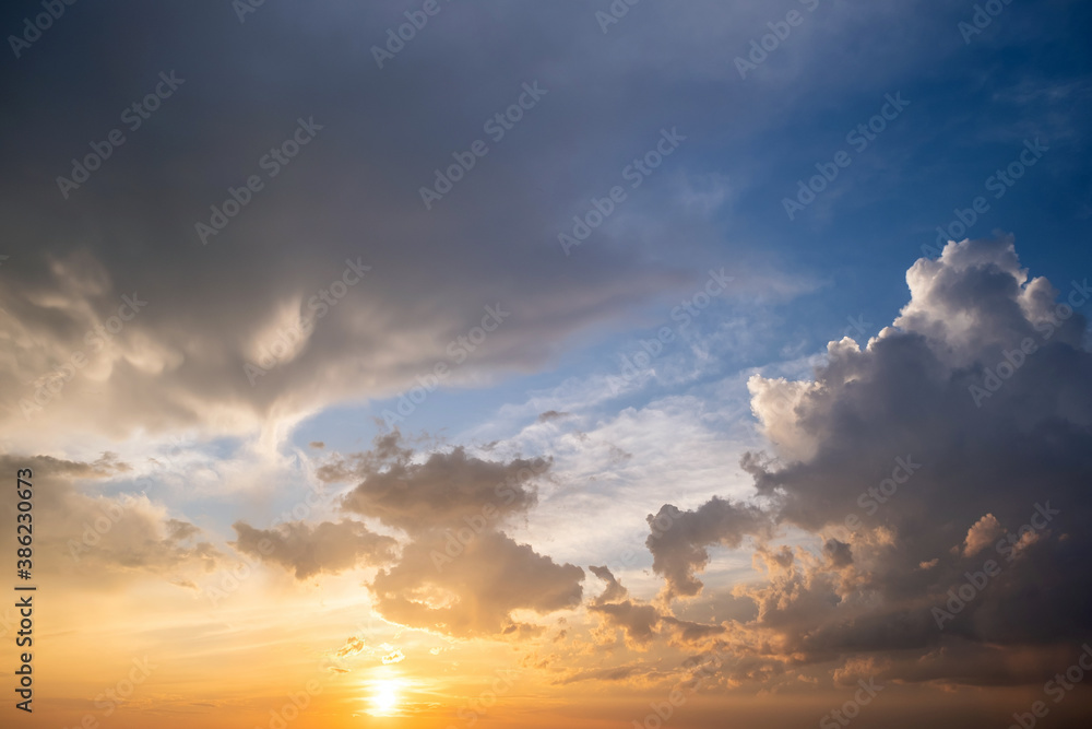 Dramatic yellow sunset landscape with puffy clouds lit by orange setting sun and blue sky.