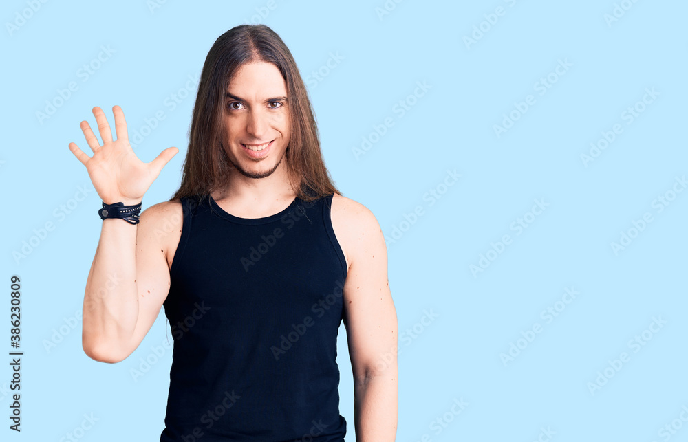 Young adult man with long hair wearing goth style with black clothes showing and pointing up with fingers number five while smiling confident and happy.