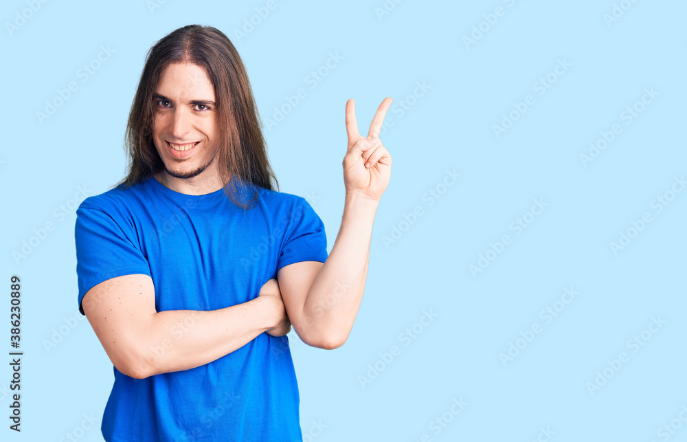 Young adult man with long hair wearing swimwear smiling with happy face winking at the camera doing victory sign. number two. Young adult man with long hair wearing swimwear smiling with happy face winking at the camera doing victory sign. number two.