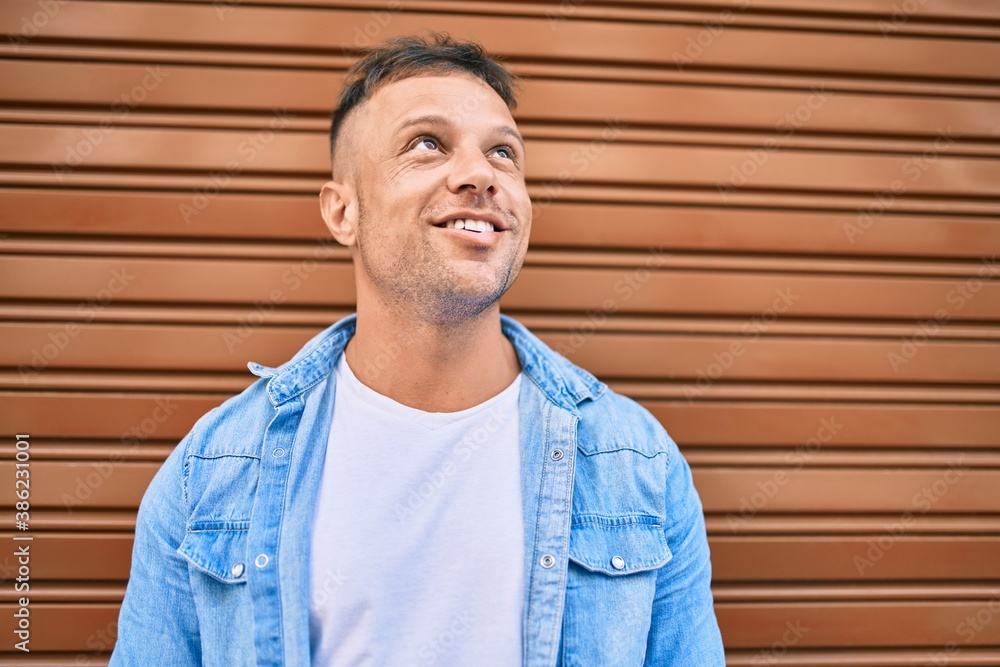 Young caucasian man smiling happy leaning on the wall at the city. Young caucasian man smiling happy leaning on the wall at the city.