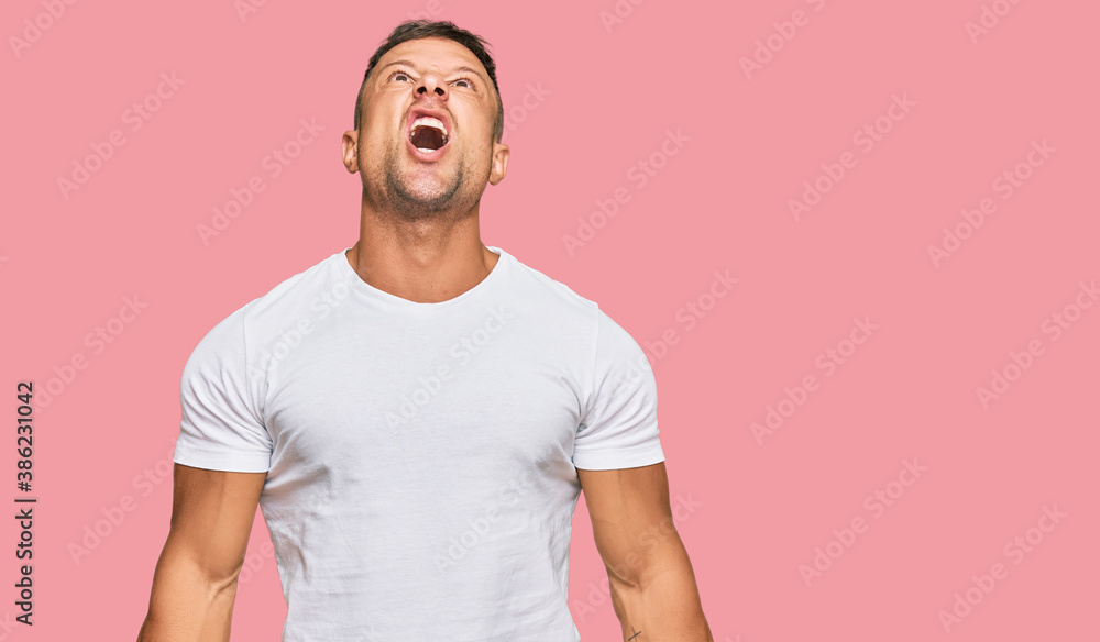 Handsome muscle man wearing casual white tshirt angry and mad screaming frustrated and furious, shouting with anger. rage and aggressive concept. Handsome muscle man wearing casual white tshirt angry and mad screaming frustrated and furious, shouting with anger. rage and aggressive concept.