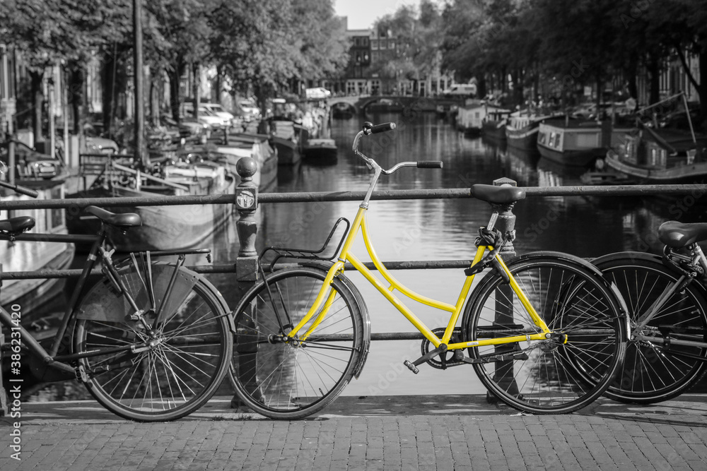 A picture of a lonely yellow bike on the bridge over the channel in Amsterdam. The background is black and white.