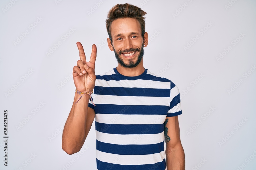 Handsome caucasian man with beard wearing casual striped t-shirt smiling with happy face winking at the camera doing victory sign. number two. Handsome caucasian man with beard wearing casual striped t-shirt smiling with happy face winking at the camera doing victory sign. number two.