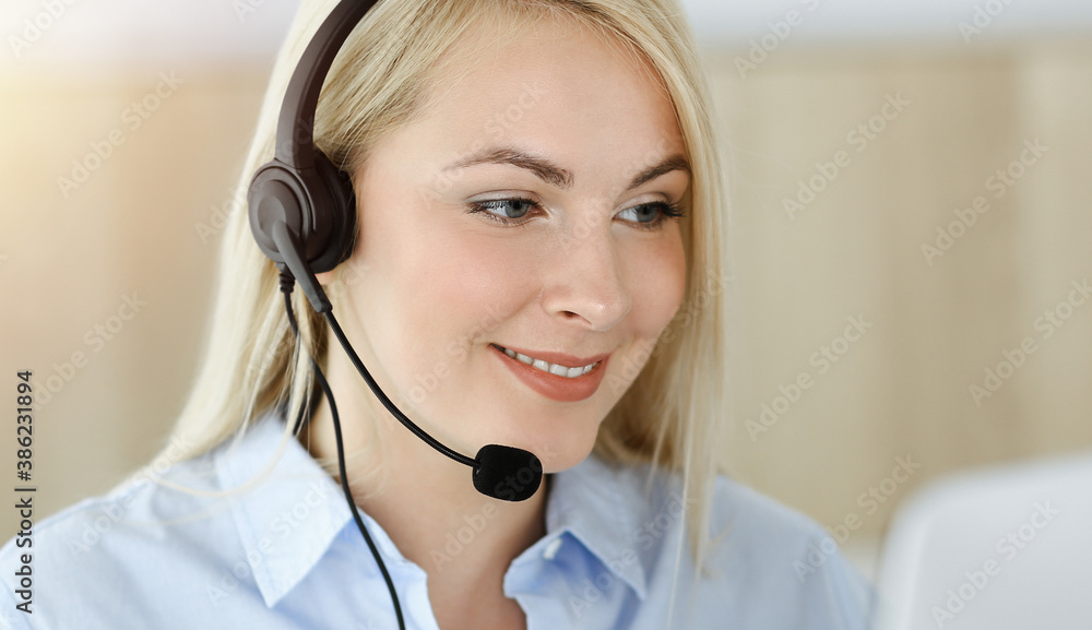 Blonde business woman sitting and communicated by headset in call center in sunny office. Concept of telesales business Blonde business woman sitting and communicated by headset in call center in sunny office. Concept of telesales business