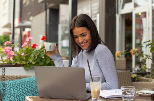 Young woman working on a laptop in a cafe and having a coffee break.