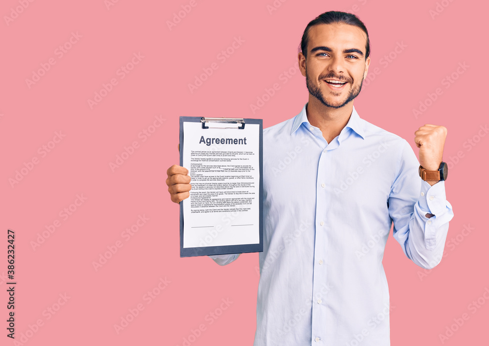 Young handsome man holding clipboard with agreement document screaming proud, celebrating victory and success very excited with raised arms Young handsome man holding clipboard with agreement document screaming proud, celebrating victory and success very excited with raised arms