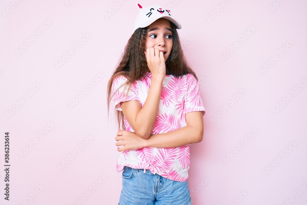 Cute hispanic child girl wearing casual clothes and funny kitty cap looking stressed and nervous with hands on mouth biting nails. anxiety problem. Cute hispanic child girl wearing casual clothes and funny kitty cap looking stressed and nervous with hands on mouth biting nails. anxiety problem.