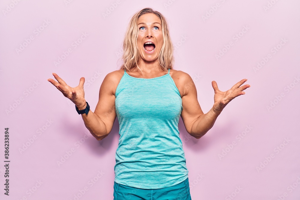 Middle age caucasian blonde woman wearing sports clothes over pink background crazy and mad shouting and yelling with aggressive expression and arms raised. frustration concept. Middle age caucasian blonde woman wearing sports clothes over pink background crazy and mad shouting and yelling with aggressive expression and arms raised. frustration concept.