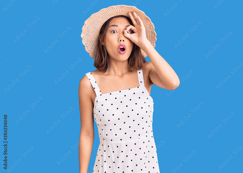 Young beautiful chinese girl wearing summer hat doing ok gesture shocked with surprised face, eye looking through fingers. unbelieving expression. Young beautiful chinese girl wearing summer hat doing ok gesture shocked with surprised face, eye looking through fingers. unbelieving expression.