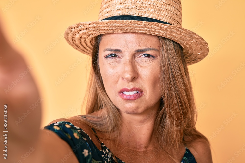 Middle age hispanic woman wearing summer hat taking a selfie clueless and confused expression. doubt concept. Middle age hispanic woman wearing summer hat taking a selfie clueless and confused expression. doubt concept.