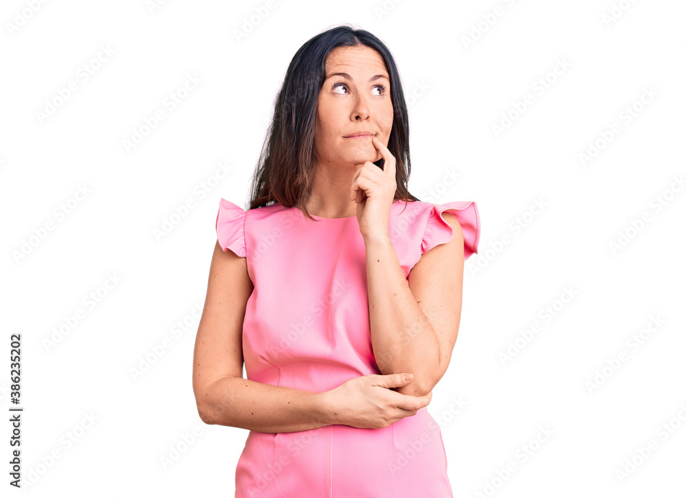Young beautiful brunette woman wearing casual dress serious face thinking about question with hand on chin, thoughtful about confusing idea Young beautiful brunette woman wearing casual dress serious face thinking about question with hand on chin, thoughtful about confusing idea