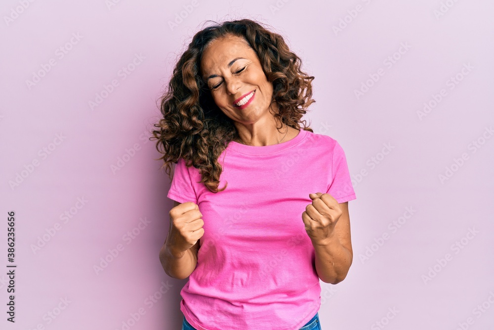 Middle age hispanic woman wearing casual clothes very happy and excited doing winner gesture with arms raised, smiling and screaming for success. celebration concept. Middle age hispanic woman wearing casual clothes very happy and excited doing winner gesture with arms raised, smiling and screaming for success. celebration concept.