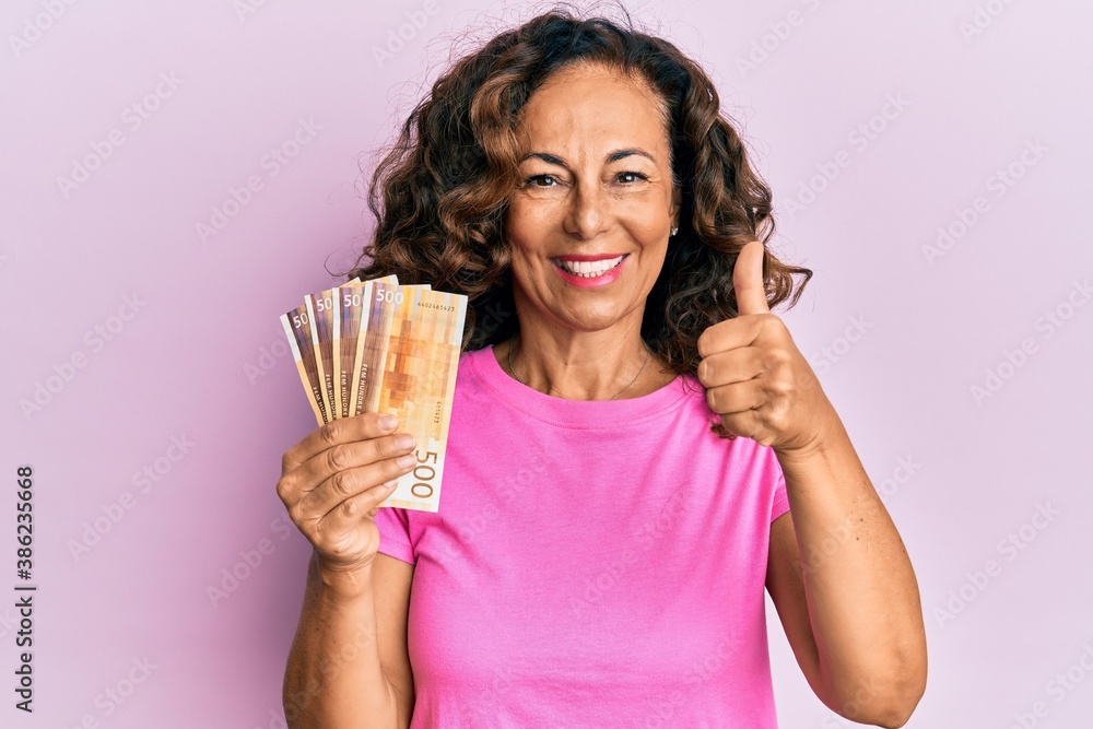 Middle age hispanic woman holding norwegian krone banknotes smiling happy and positive, thumb up doing excellent and approval sign Middle age hispanic woman holding norwegian krone banknotes smiling happy and positive, thumb up doing excellent and approval sign