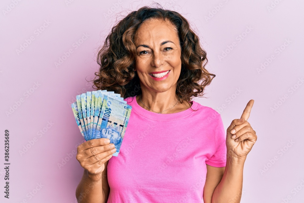Middle age hispanic woman holding south african 20 rand banknotes smiling happy pointing with hand and finger to the side Middle age hispanic woman holding south african 20 rand banknotes smiling happy pointing with hand and finger to the side