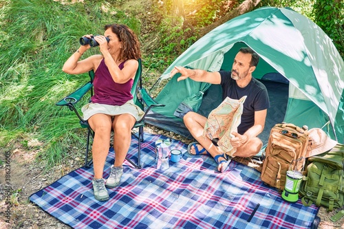 Middle age couple  of hiker camping at the forest. Smiiling happy using binoculars pointing to the side with finger. photo