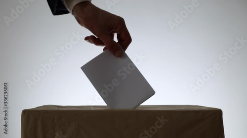 Man's hand throws a ballot paper for voting at a polling station during elections.