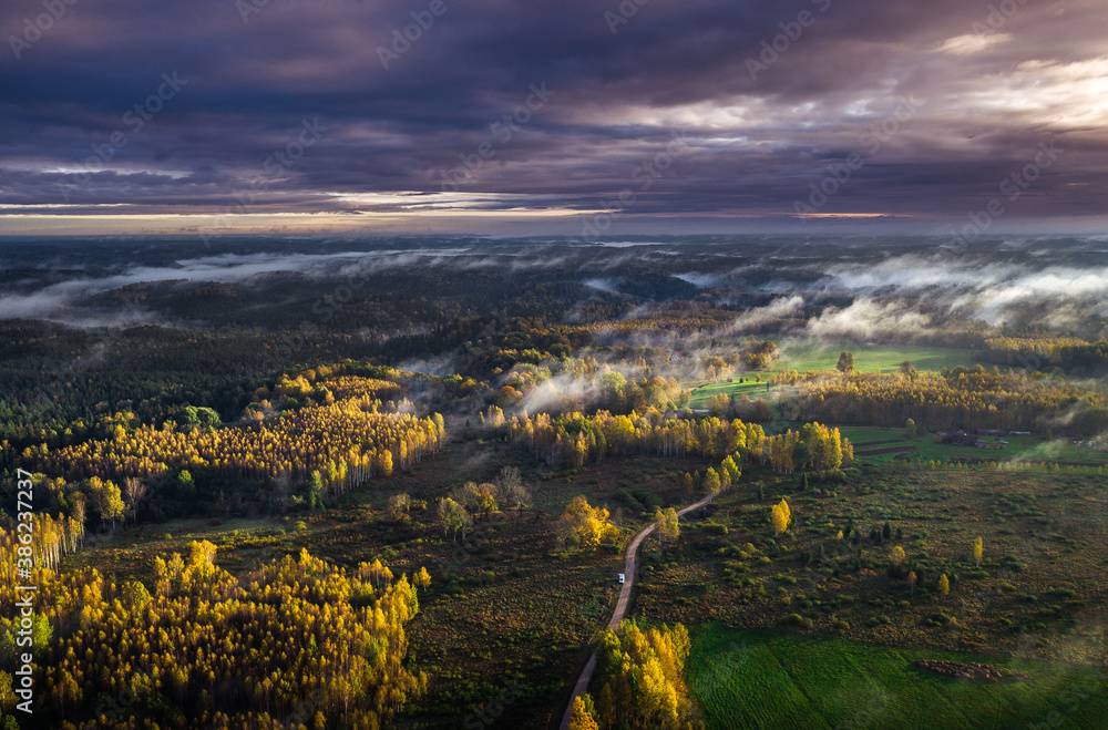 Epic sunrise over the foggy valley in autumn. Morning light lightens colorful forest covered in mist. Impressive storm clouds. 