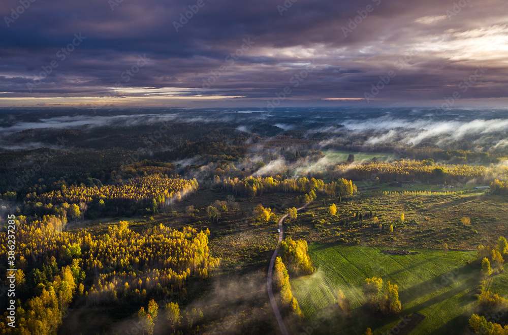 Fototapeta premium Epic sunrise over the foggy valley in autumn. Morning light lightens colorful forest covered in mist. Impressive storm clouds. 