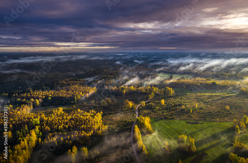 Epic sunrise over the foggy valley in autumn. Morning light lightens colorful forest covered in mist. Impressive storm clouds. 