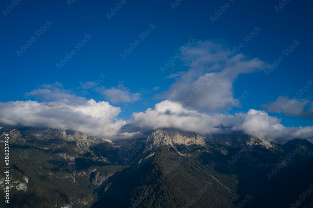 High mountains in the Europe. Panorama of beautiful countryside of Italy. Clouds on top of the Alps, blue sky. Idyllic landscape in the Alps.