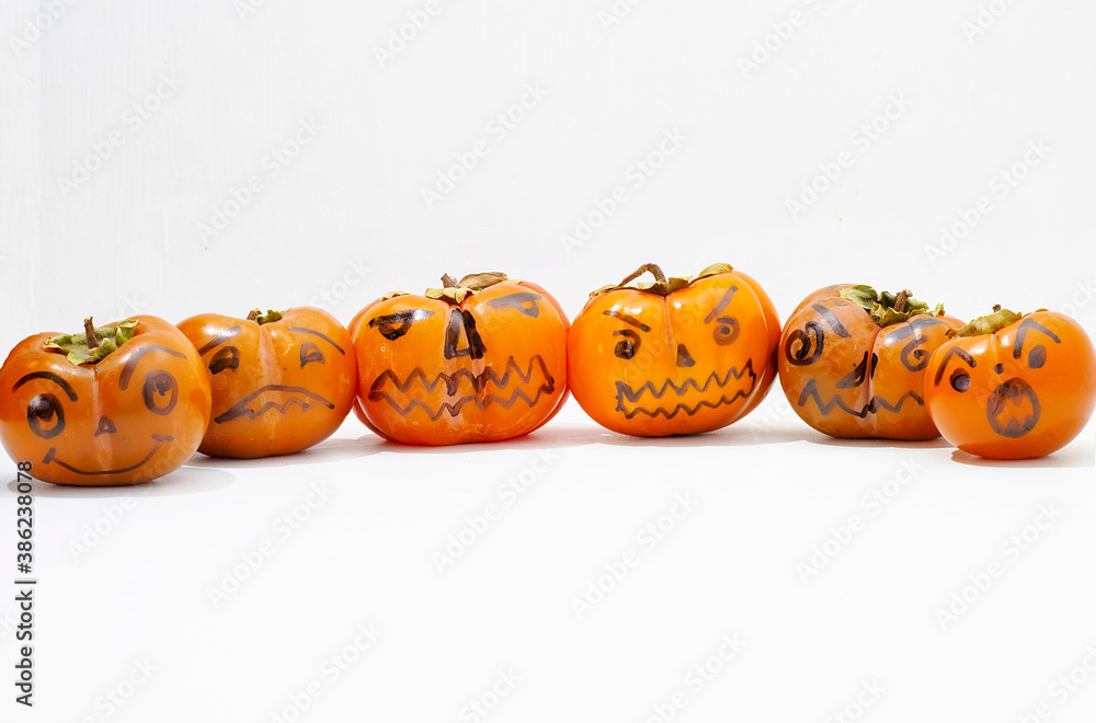 Jack - o ' - lantern, Halloween monsters - muzzles drawn on persimmon fruit. Persimmon is very similar to a pumpkin, the same orange and cheerful. Jack - o ' - lantern, Halloween monsters - muzzles drawn on persimmon fruit. Persimmon is very similar to a pumpkin, the same orange and cheerful.