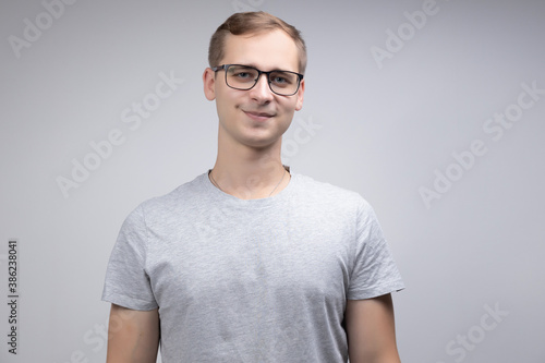 Close-up portrait of a smiling business man with glasses looking at the camera with a smile isolated on a white-gray background © vitalii_demin
