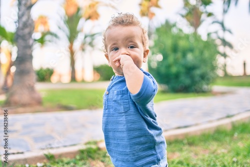 Sad little boy putting fingers on mouth touching gums because toothache at the park on a sunny day. Beautiful blonde hair male toddler in pain for new baby teeth outdoors © Krakenimages.com