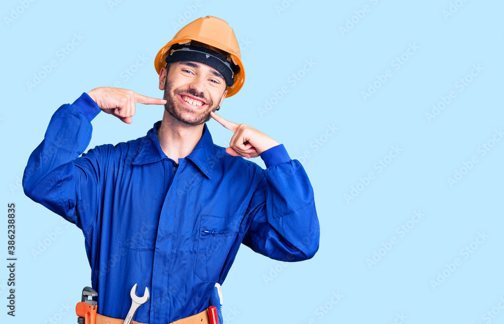 Young hispanic man wearing worker uniform smiling cheerful showing and pointing with fingers teeth and mouth. dental health concept.