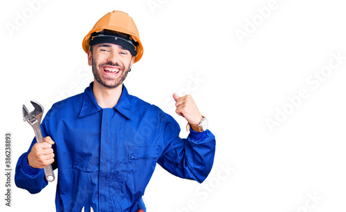 Young hispanic man wearing electrician uniform holding wrench screaming proud, celebrating victory and success very excited with raised arms photo