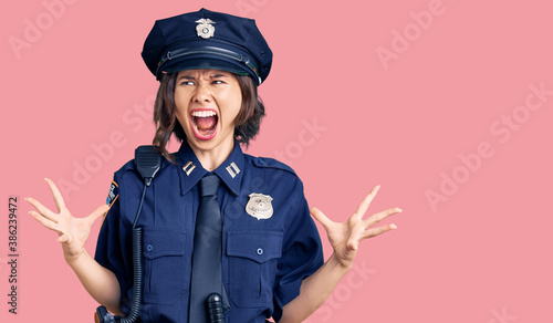 Young beautiful girl wearing police uniform crazy and mad shouting and yelling with aggressive expression and arms raised. frustration concept.