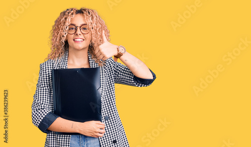 Fotografi Young blonde woman with curly hair holding business folder smiling happy and pos
