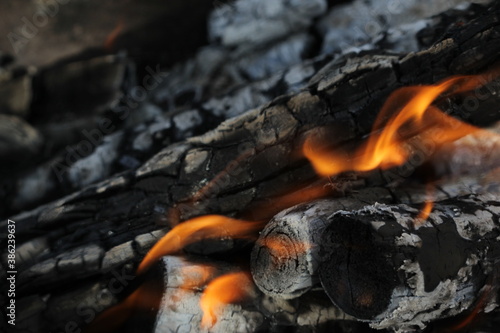 Smoldered logs burned in vivid fire close up. Atmospheric background with flame of campfire. Unimaginable detailed image of bonfire from inside with copy space. Whirlwind of smoke and glowing embers.