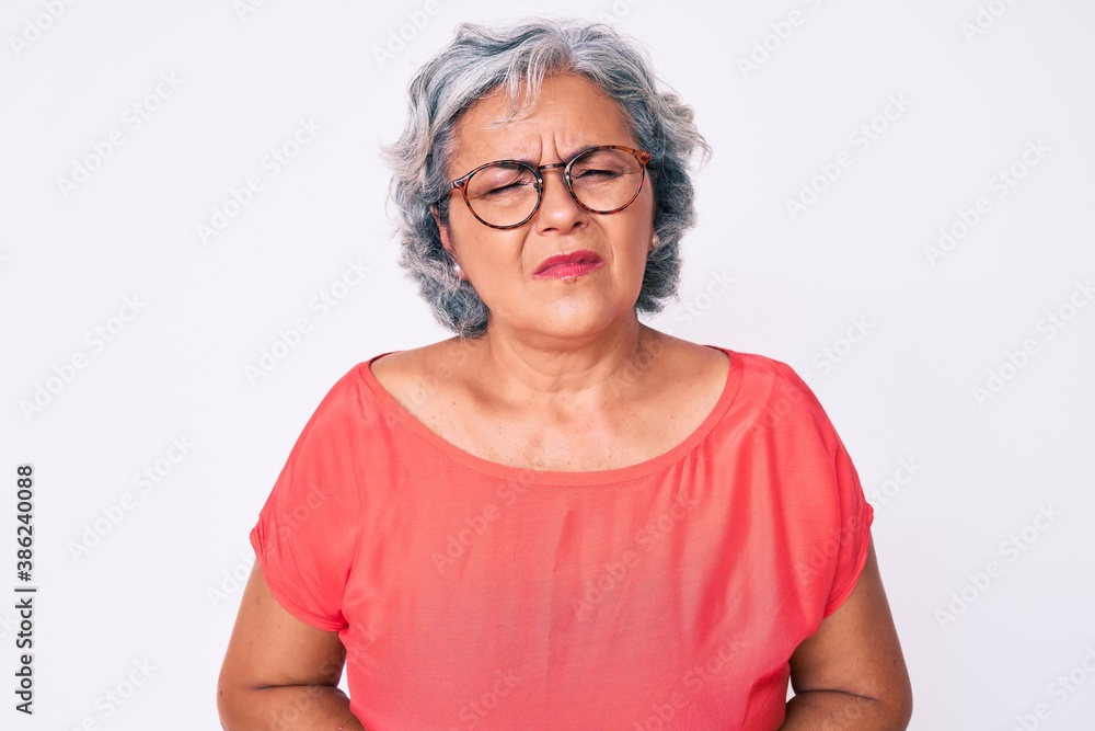 Senior hispanic grey- haired woman wearing casual clothes and glasses with hand on stomach because nausea, painful disease feeling unwell. ache concept. Senior hispanic grey- haired woman wearing casual clothes and glasses with hand on stomach because nausea, painful disease feeling unwell. ache concept.