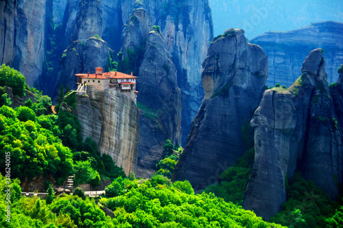 Beautiful scenic view, Holy Orthodox Monastery of Rousanou (St. Barbara) on the top of monolithic pillar, green foliage, huge barren rocks in Meteora, Pindos Mountains, Thessaly, Greece, Europe