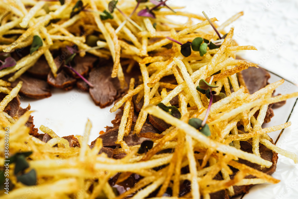 slices of baked beef on a white plate with thin strips of fried potatoes slices of baked beef on a white plate with thin strips of fried potatoes