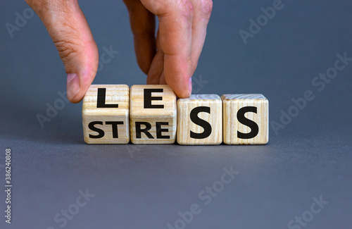 Having less stress or being stress-less. The word 'STRESS' and 'LESS' on wooden cubes. Male hand.  Beautiful grey background, copy space.