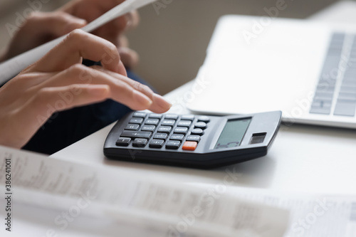 Crop close up of woman calculate expenses expenditures on calculator machine managing family budget at home. Female pay bills taxes online, consider household financial documents, make savings.