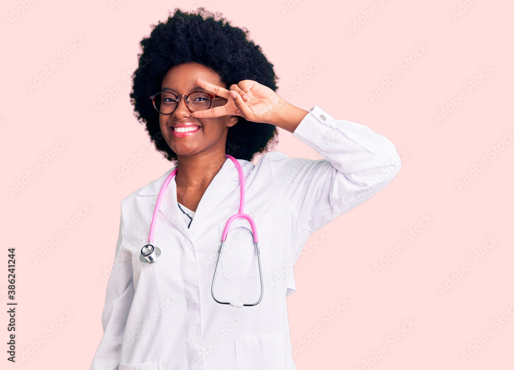 Young african american woman wearing doctor coat and stethoscope doing peace symbol with fingers over face, smiling cheerful showing victory Young african american woman wearing doctor coat and stethoscope doing peace symbol with fingers over face, smiling cheerful showing victory