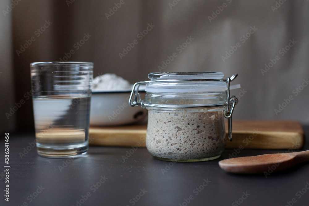 Active rye sourdough starter in a jar, a glass of water and a bowl with flour. Active rye sourdough starter in a jar, a glass of water and a bowl with flour.