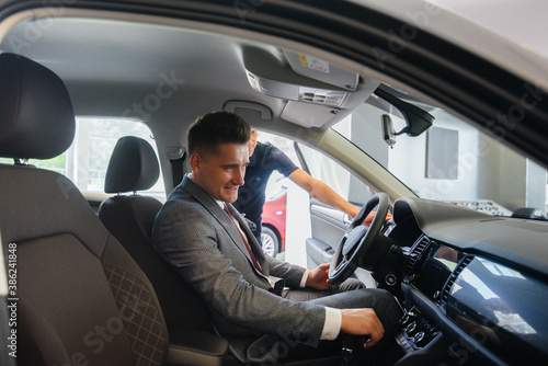 A young businessman with a salesman looks at a new car in a car dealership. Buying a car