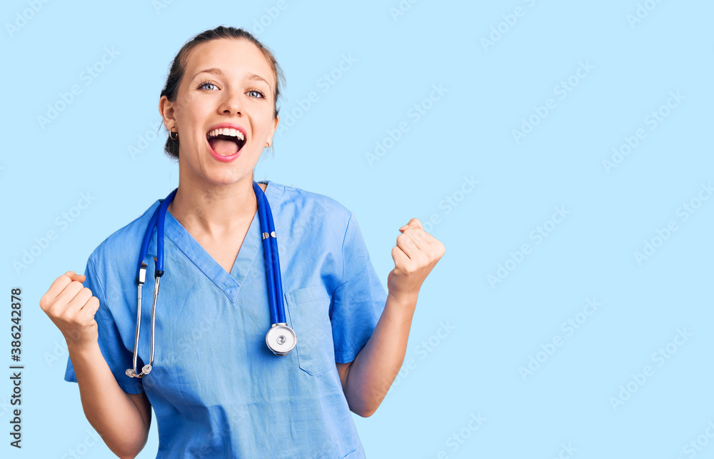 Young beautiful blonde woman wearing doctor uniform and stethoscope celebrating surprised and amazed for success with arms raised and open eyes. winner concept. Young beautiful blonde woman wearing doctor uniform and stethoscope celebrating surprised and amazed for success with arms raised and open eyes. winner concept.