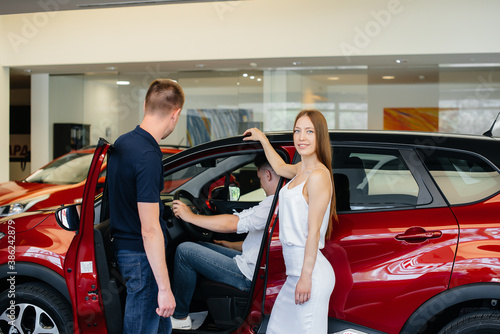A happy young couple chooses and buys a new car at a car dealership. Buying a new car