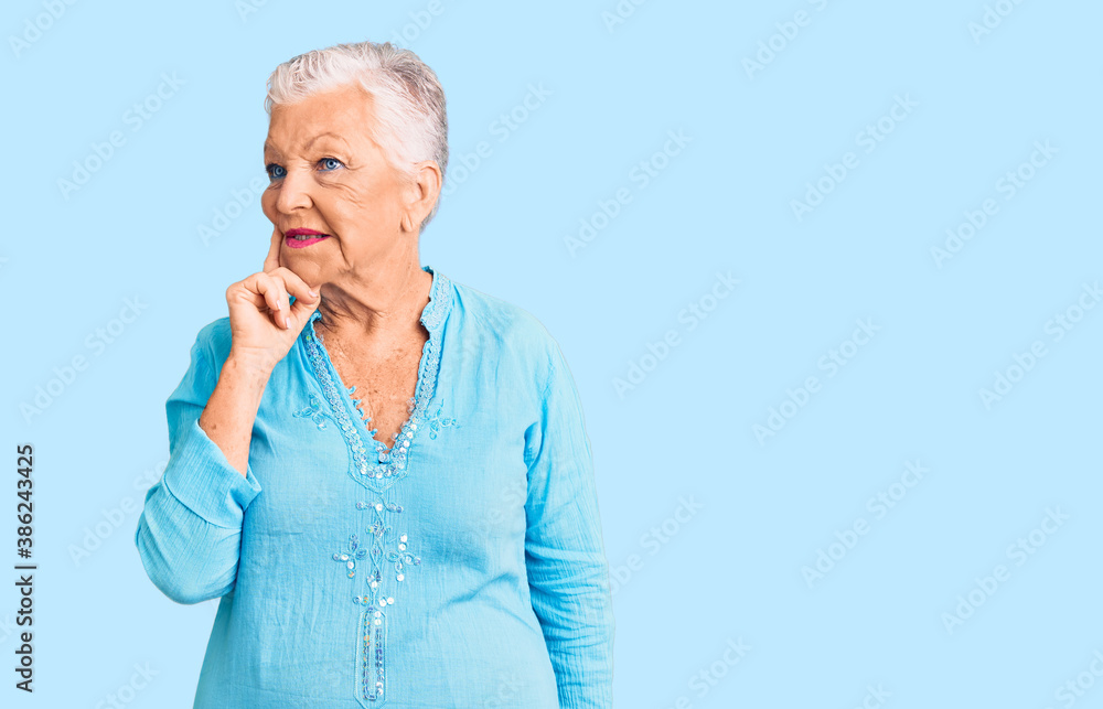 Senior beautiful woman with blue eyes and grey hair wearing summer dress with hand on chin thinking about question, pensive expression. smiling with thoughtful face. doubt concept. Senior beautiful woman with blue eyes and grey hair wearing summer dress with hand on chin thinking about question, pensive expression. smiling with thoughtful face. doubt concept.